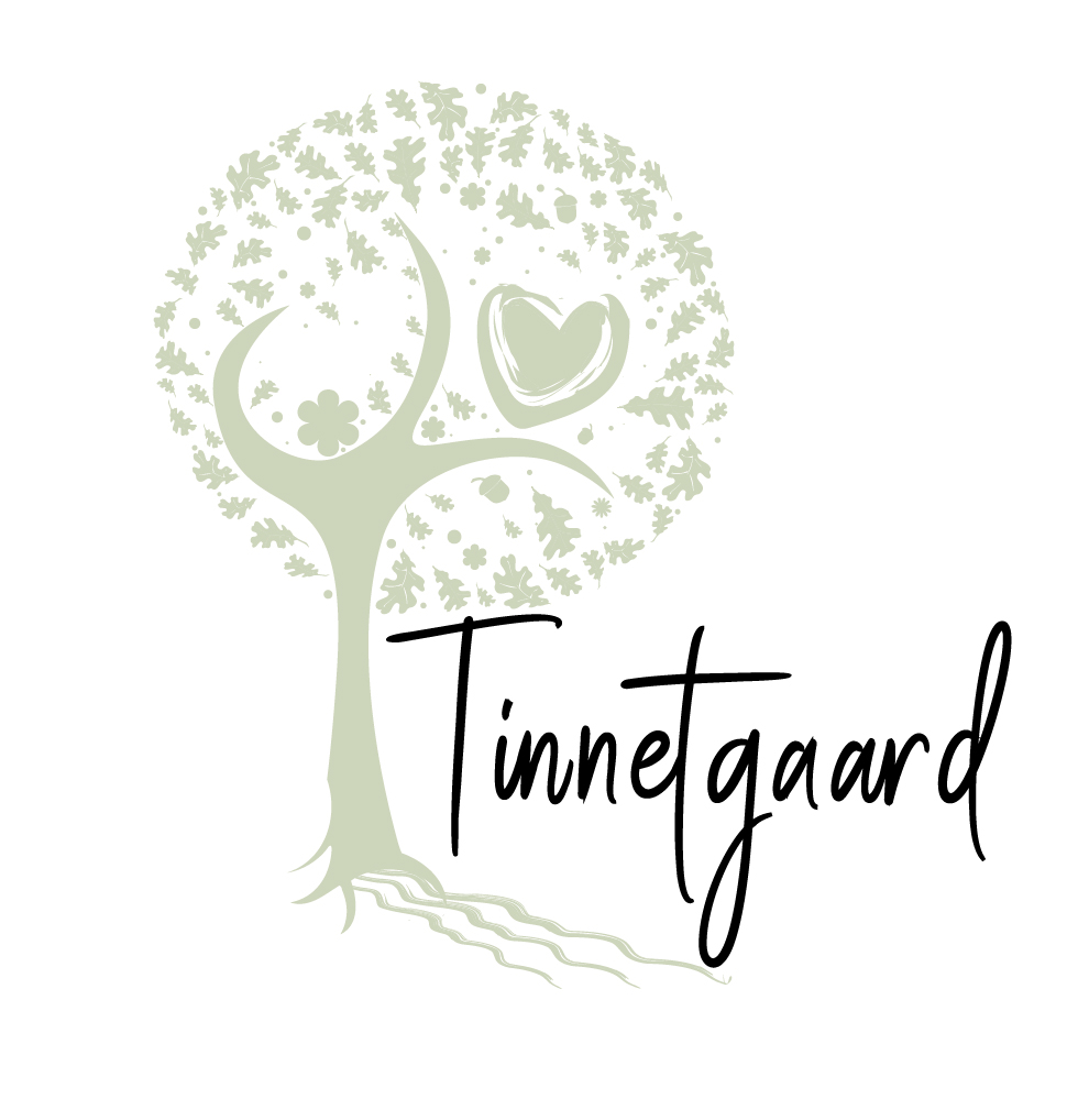 Stiliseret lysegrønt træ med rund krone dannet af små blade og blomster samt et hjerte i kronen, rødder der strækker sig nedad, og foran står teksten "Tinnetgaard" i sort håndskrift.